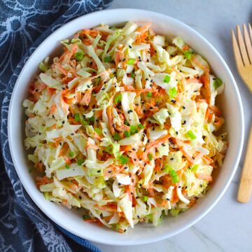 Coleslaw with an asian salad dressing recipe and black sesame seeds on top in a bowl. It has cabbage, carrots, scallions, and sesame seeds in a creamy dressing with mayonnaise. vinegar, soy sauce, and Sesame Oil.  It really is a sidekick that can go with anything!