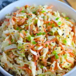 Coleslaw with an asian salad dressing recipe and black sesame seeds on top in a bowl. It has cabbage, carrots, scallions, and sesame seeds in a creamy dressing with mayonnaise. vinegar, soy sauce, and Sesame Oil.  It really is a sidekick that can go with anything!