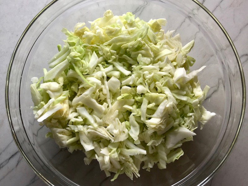 Thinly sliced cabbage thin for Asian Coleslaw. It has cabbage, carrots, scallions, and sesame seeds in a creamy dressing with mayonnaise. vinegar, soy sauce, and Sesame Oil.  It really is a sidekick that can go with anything!