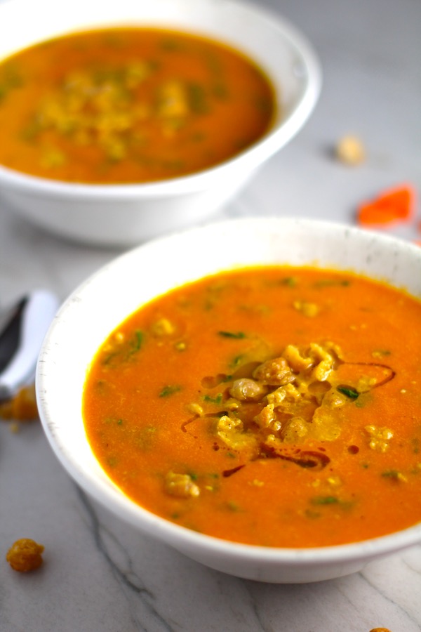 Carrot and chickpea Soup close up in a bowl with a another bowl in back. Creamy Carrot Soup with Kale, Roasted Chickpeas and Thyme is a creamy, textured, easy-to-make soup! It's great as a starter, but hearty enough to be a meal with Kale and Chickpeas. Not only does this soup taste delicious, it's also incredibly healthy with vitamins, nutrients, fiber, and protein!