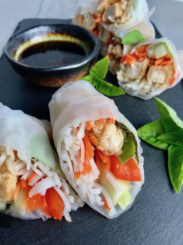 Teriyaki Chicken Summer Rolls with carrots, basil, red pepper and rice noodles inside, cut in half and stacked on slate platter with Garlic Honey Soy Dipping Sauce.  Easy, fun, and delicious! 