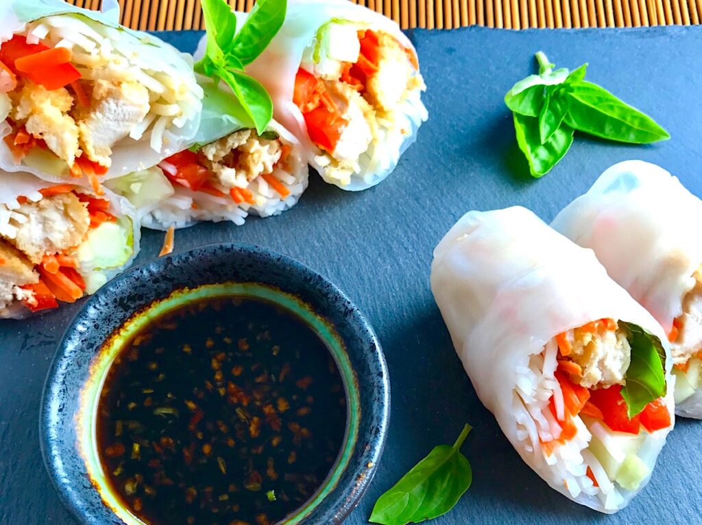 Teriyaki Chicken Summer Rolls with carrots, basil, red pepper and rice noodles inside, cut in half and stacked on slate platter with Garlic Honey Soy Dipping Sauce. Easy, fun, and delicious!