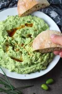 Edamame Dip with Gorgonzola and Harissa Oil drizzled on top on a plate with bread. It's creamy, savory, nutty, and utterly delicious!