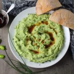 Edamame Dip with Gorgonzola and Harissa Oil drizzled on top on a plate with bread. It's creamy, savory, nutty, and utterly delicious!