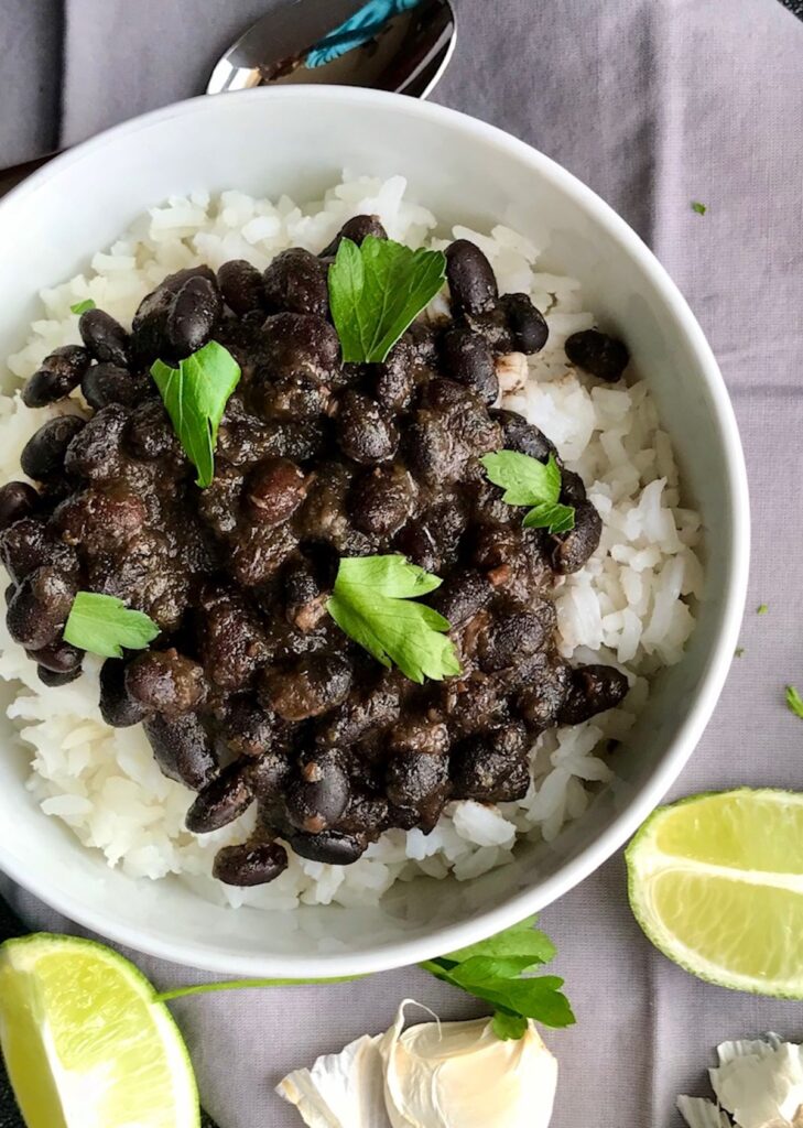 Slow Cooker Brazilian Beans and rice in a bowl with cilantro on top and lime wedges on the counter. These black beans are thick, rich, and delicious! Serve as a side or main over rice.