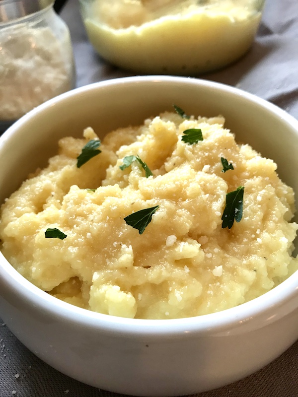 Creamy Parmesan Polenta in a bowl with grated parmesan and parsley garnish and parmesan bottle in background.