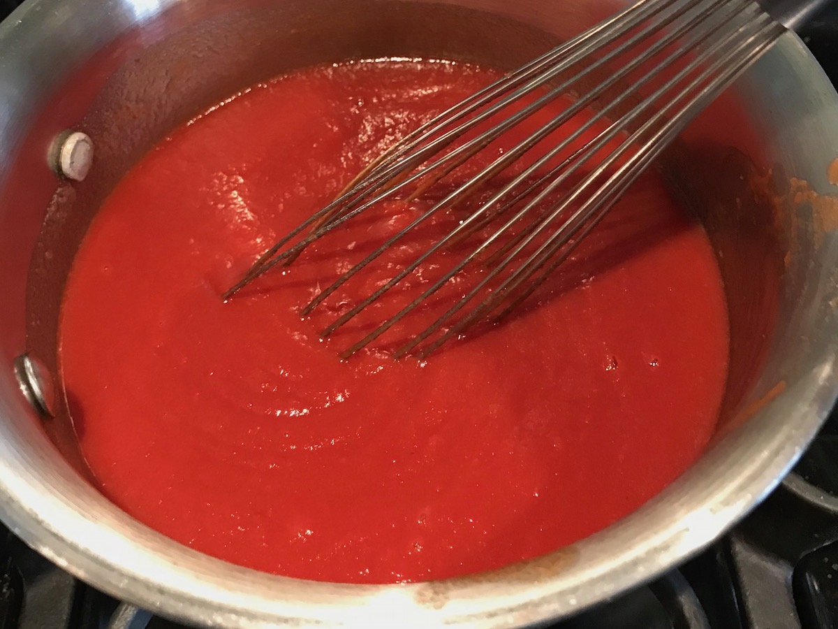 Whisk mixing ketchup ingredients in pot for the Best Honey Ketchup recipe.