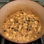 Creamy Cajun Cauliflower and Beans in a pot with wood spoon. The mild cajun flavors combined with  healthy garbanzo beans, black beans, cauliflower, and mushrooms make this a hearty, creamy, and delicious dish