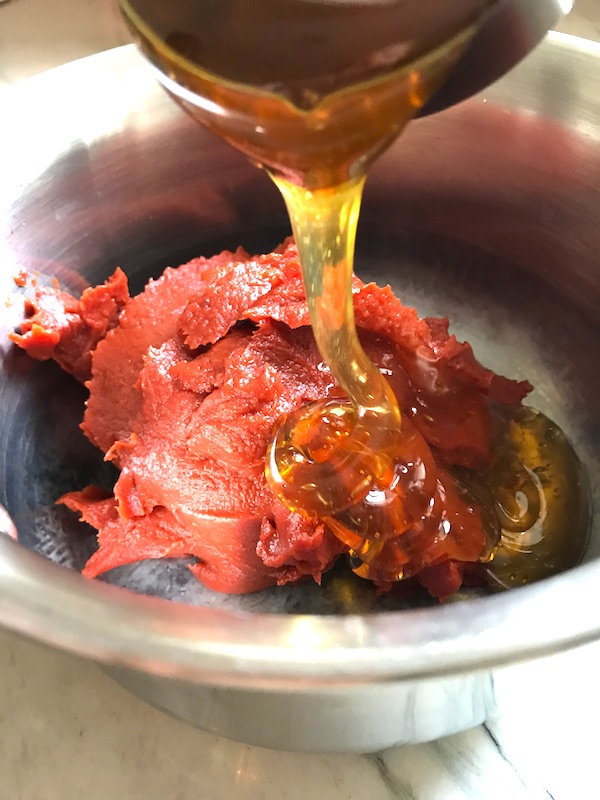 Honey pouring over tomato paste in pot for the Best Sugar Free Ketchup.