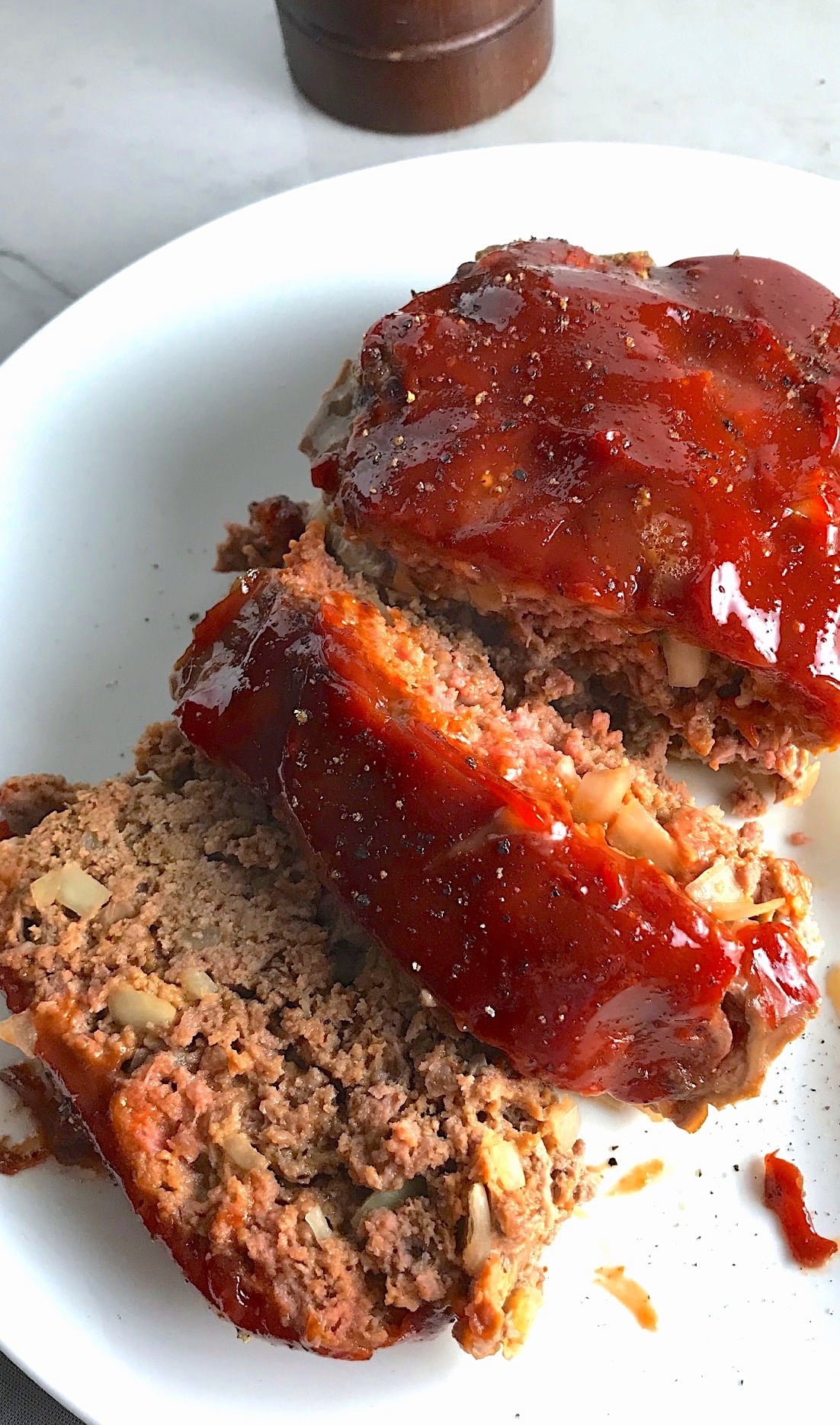 Overhead picture of sliced meatloaf with ketchup on top on a plate. This 5-Ingredient Easy Meatloaf recipe may be short on ingredients, but it is loaded with flavor. The lack of breadcrumbs means you don't have them soaking up the juices, so the meat stays moist - and it's gluten free too! Parmesan cheese, onion, egg, ketchup, salt, and pepper are all that go into this yummy loaf of goodness!