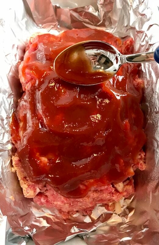 Raw meatloaf with ketchup on top in aluminum lined loaf pan. This 5-Ingredient Easy Meatloaf recipe may be short on ingredients, but it is loaded with flavor. The lack of breadcrumbs means you don't have them soaking up the juices, so the meat stays moist - and it's gluten free too! Parmesan cheese, onion, egg, ketchup, salt, and pepper are all that go into this yummy loaf of goodness!