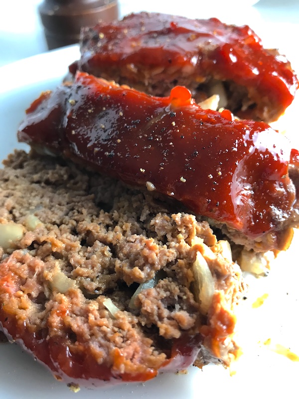 Close up picture of sliced meatloaf with ketchup on top. This 5-Ingredient Easy Meatloaf recipe may be short on ingredients, but it is loaded with flavor. The lack of breadcrumbs means you don't have them soaking up the juices, so the meat stays moist - and it's gluten free too! Parmesan cheese, onion, egg, ketchup, salt, and pepper are all that go into this yummy loaf of goodness!