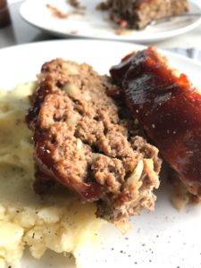 Close up picture of sliced meatloaf with ketchup on top with mashed potatoes on plate. This 5-Ingredient Easy Meatloaf recipe may be short on ingredients, but it is loaded with flavor. The lack of breadcrumbs means you don't have them soaking up the juices, so the meat stays moist - and it's gluten free too! Parmesan cheese, onion, egg, ketchup, salt, and pepper are all that go into this yummy loaf of goodness!