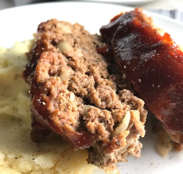 Close up picture of sliced meatloaf with ketchup on top with mashed potatoes on plate. This 5-Ingredient Easy Meatloaf recipe may be short on ingredients, but it is loaded with flavor. The lack of breadcrumbs means you don't have them soaking up the juices, so the meat stays moist - and it's gluten free too! Parmesan cheese, onion, egg, ketchup, salt, and pepper are all that go into this yummy loaf of goodness!