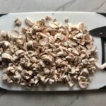 Chopped white button mushrooms on a cutting board for Creamy Parmesan Mushroom Quinoa Risotto.