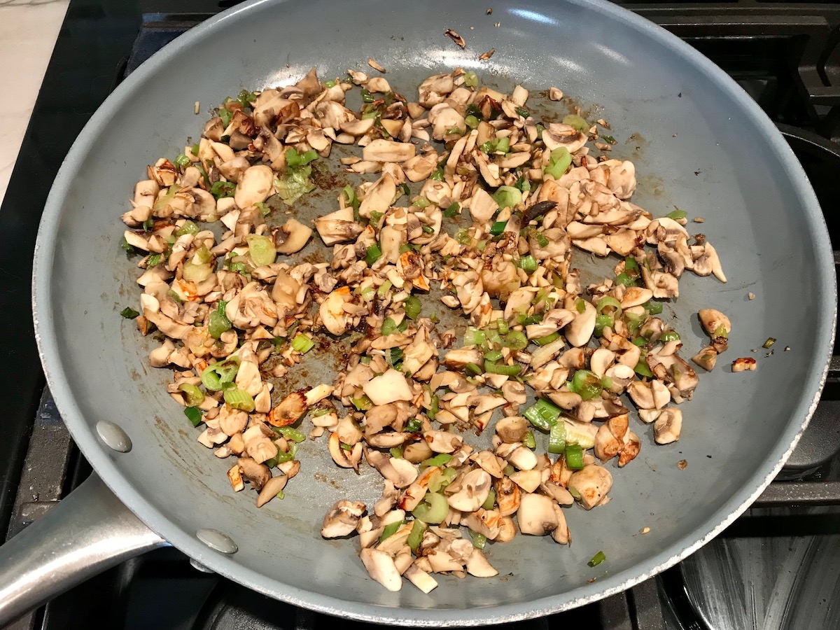 Chopped white button mushrooms cooking in a frying pan with scallions for Creamy Parmesan Mushroom Quinoa Risotto