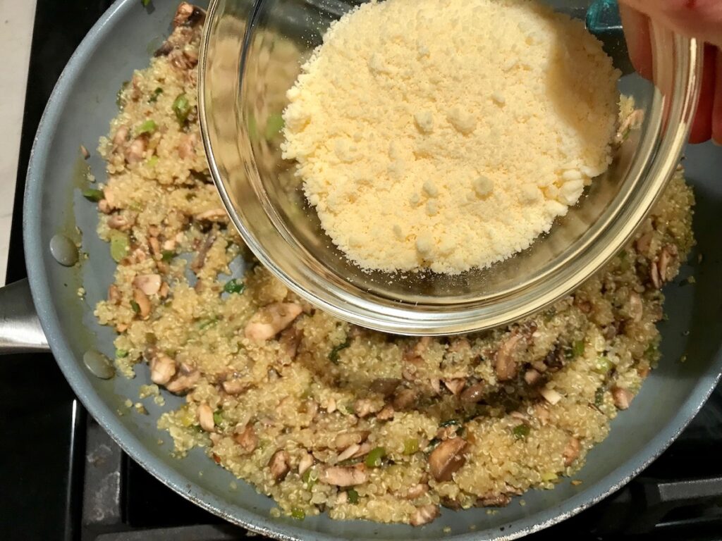 Bowl of grated parmesan cheese being added mushroom Quinoa risotto in frying pan for Creamy Parmesan Mushroom Quinoa Risotto