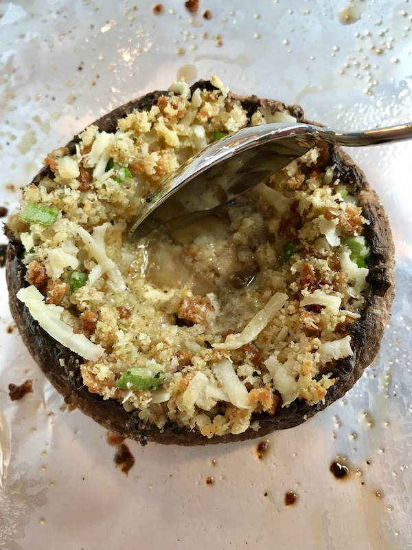 Spoon pressing in the filling in the Portabella Mushroom Egg Nests on pan. Portabella mushrooms are filled with garlic, scallion, breadcrumb & Manchego cheese stuffing!  Then an egg is baked nestled in the center of all of this goodness.