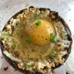 Uncooked Portabella Mushroom Egg Nests on pan. Portabella mushrooms are filled with garlic, scallion, breadcrumb & Manchego cheese stuffing!  Then an egg is baked nestled in the center of all of this goodness.