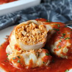 Stuffed Cabbage Rolls on a plate with one cut open. They're a great make-ahead family dish! This recipe uses ground chicken, paprika, parmesan, tomato paste, garlic, and onion for tons of flavor!