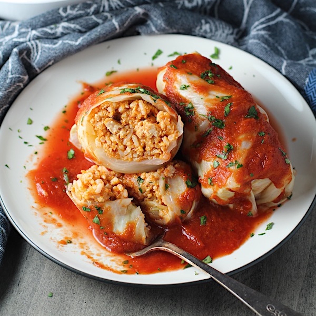 Stuffed Cabbage Rolls on a plate with one cut open. They're a great make-ahead family dish! This recipe uses ground chicken, paprika, parmesan, tomato paste, garlic, and onion for tons of flavor!