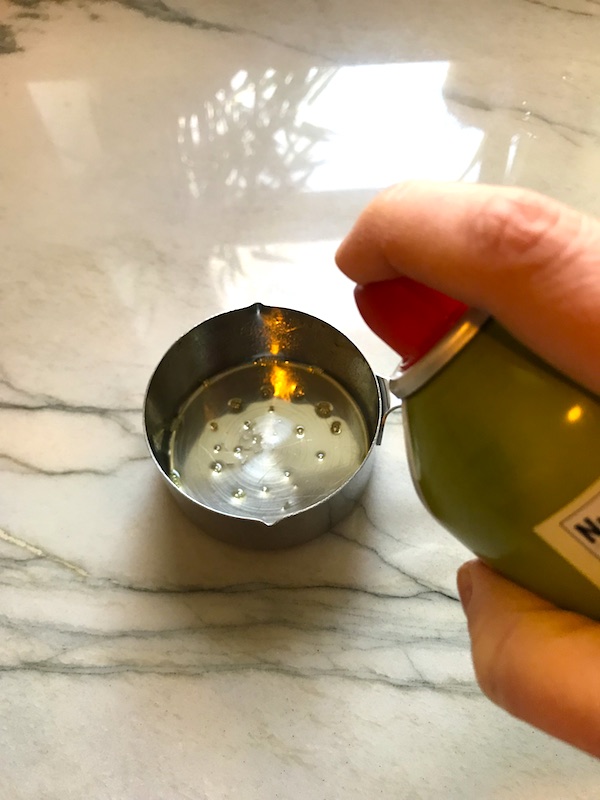 Hand spraying olive oil into a measuring cup for Best Sugar Free Ketchup.