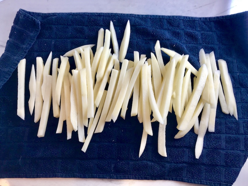 Raw potatoes cut into fries on a towel to be dried for baking with Crispy Baked Cod Panko Fish and Chips.