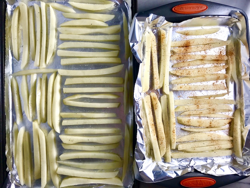 Raw potatoes cut into fries and seasoned and lined up on a sheet pan lined with aluminum foil to be baked for Crispy Baked Cod Panko Fish and Chips.
