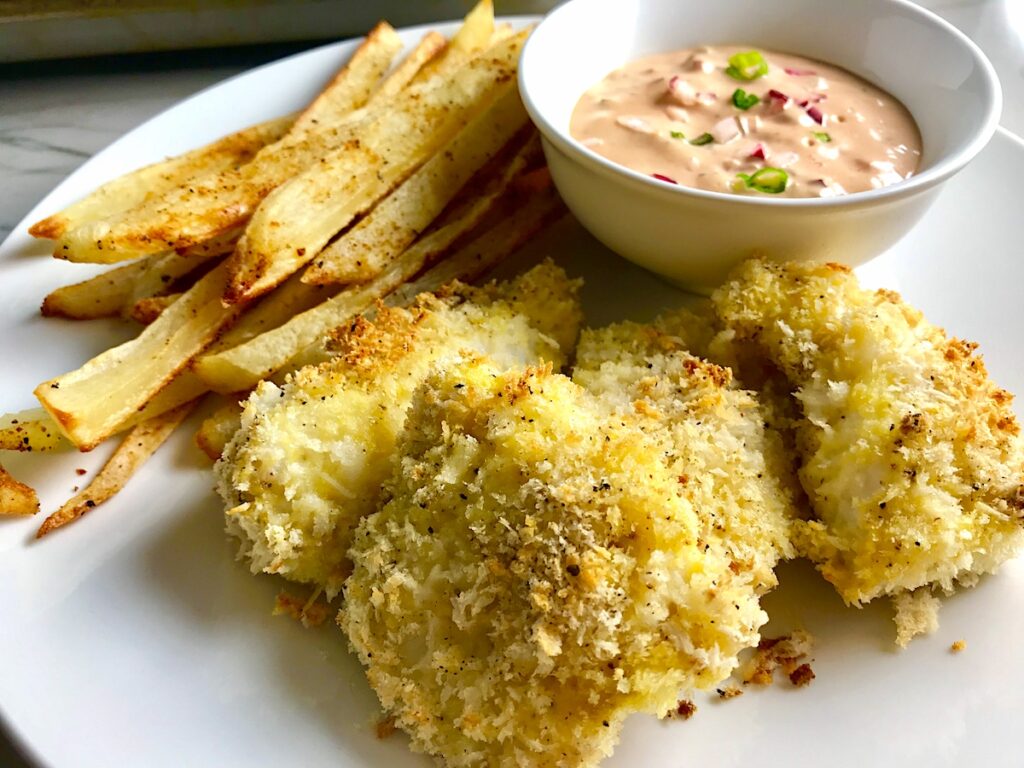 Crispy Baked Cod Panko Fish and Chips on a plate with side of remoulade dipping sauce. Everything bakes in the oven on a sheet pan to save time and energy.