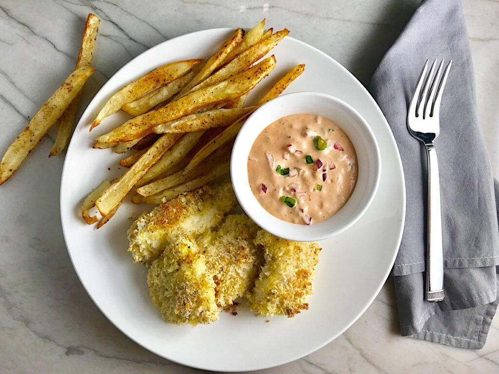 Crispy Baked Cod Panko Fish and Chips on a plate with side of remoulade dipping sauce. Everything bakes in the oven on a sheet pan to save time and energy.