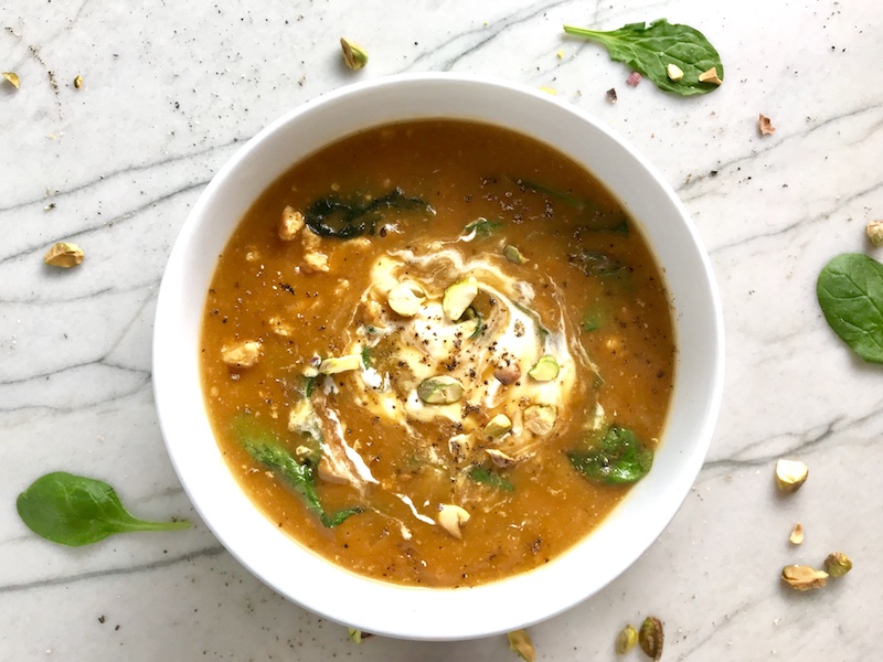 Creamy Tomato Soup with Ground Chicken and Spinach in a pot on counter with spoon and spinach leaves on counter. It