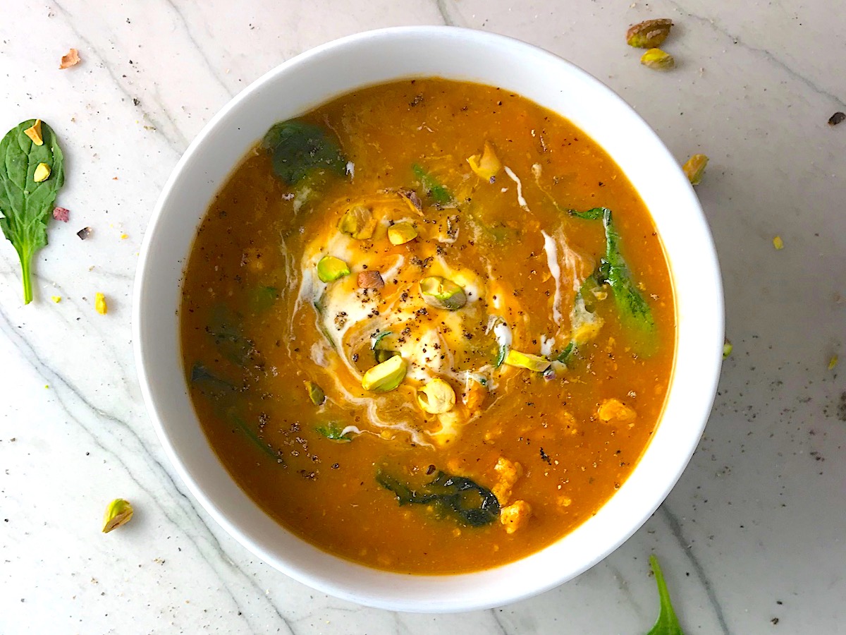 Creamy Tomato Soup with chicken in a white bowl on counter with spinach and sour cream and pistachios on top.