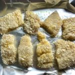 Raw cod fish breaded on a sheet pan lined with aluminum before being baked for Crispy Baked Cod Panko Fish and Chips.