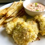 Crispy Baked Cod Panko Fish and Chips on a plate with side of remoulade dipping sauce and pan in background. Everything bakes in the oven on a sheet pan to save time and energy.