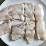 Raw cod fish cut into large pieces on a plate for Crispy Baked Cod Panko Fish and Chips.