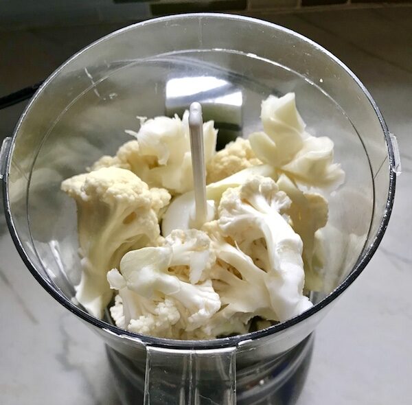 Cauliflower florets in a food processor for Cheesy Cauliflower Rice recipe.
