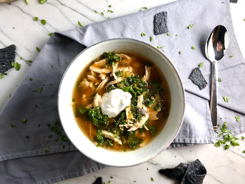 Chicken Tortilla Soup in a bowl with sour cream on top and tortilla chips on side. It's quick, it's easy, it's delicious AND...it's an all-in-one balanced dish because I have added KALE! Done in 30 minutes!