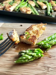 Parmesan breadcrumb chicken on cutting board with bite on fork and asparagus cut.