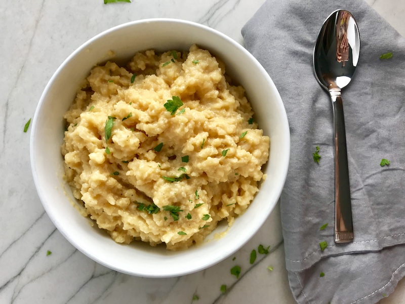 Cheesy Cauliflower Rice in a bowl with parsley garnish and napkin with spoon to the side.