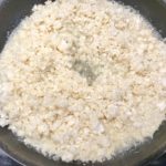 Cauliflower rice cooking in a skillet with broth for Cheesy Cauliflower Rice.