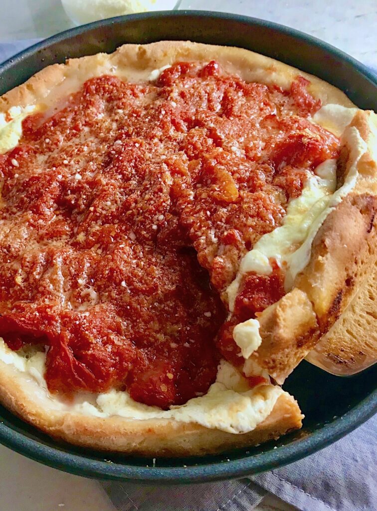 Spatula lifting slice Chicago Style deep dish pizza with chicken sausage and tomatoes on top from a round pan.