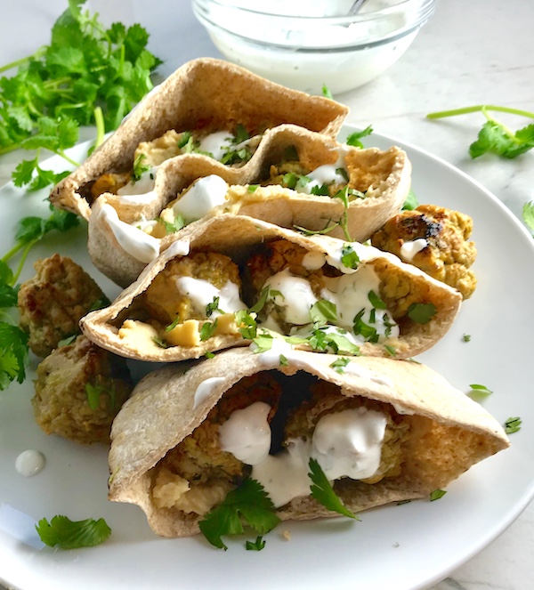 Moroccan Meatball Stuffed Pitas on a plate. They are filled with homemade hummus, moist turkey meatballs made with warm Moroccan spices like ginger, turmeric, and coriander, and then topped with creamy, fresh and bright lemon yogurt sauce.