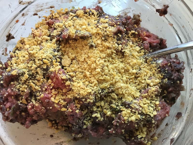 Raw ground beef in a bowl with tortilla chip crumbs on top for Chipotle Meatballs with Mexican Corn Cream Sauce
