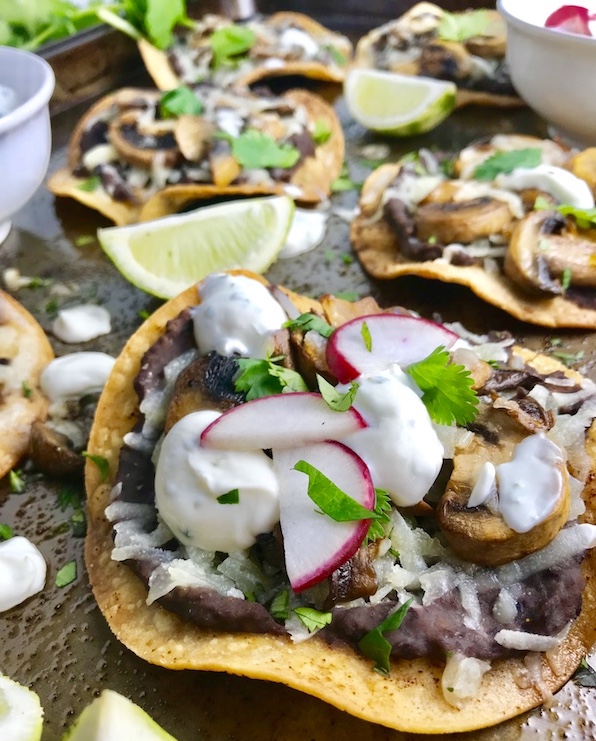 Mushroom and Black Bean Tostadas with Manchego Cheese, and Cilantro Lime Cream are crazy good! The tortillas are baked until crunchy, then topped with homemade refried black beans, nutty aged Manchego Cheese, sautéed mushrooms, and then baked until the cheese is melted. Top with cool cilantro lime cream, crisp radishes, and fresh cilantro. Simple, Gluten-Free, Vegetarian, Delicious!