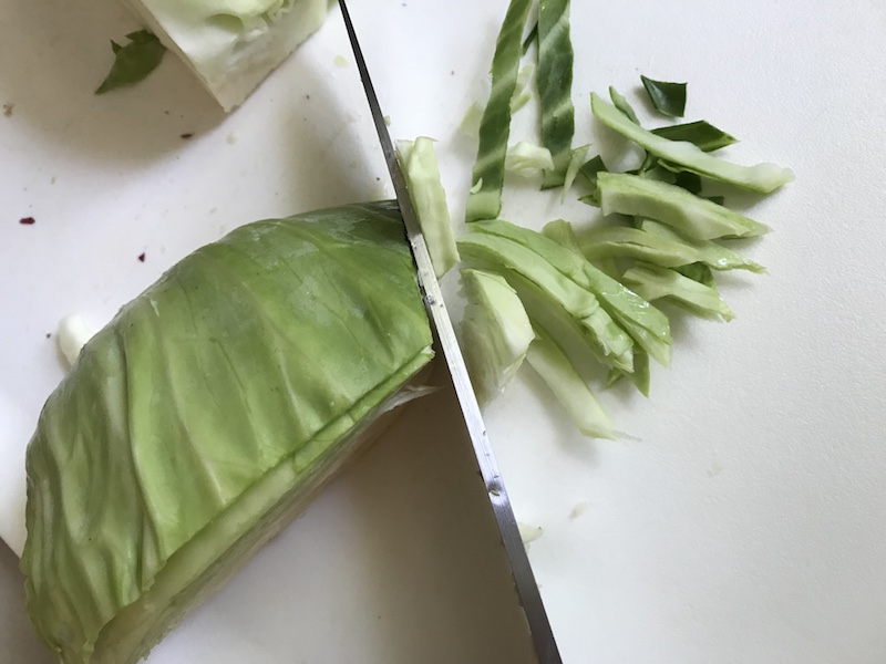 Cabbage being sliced thin on a cutting board for Healthy Chicken Ramen Noodle bowls with flavorful broth, hearty chicken, crunchy veggies, creamy egg, sesame seeds & scallions.  Gluten-Free too!