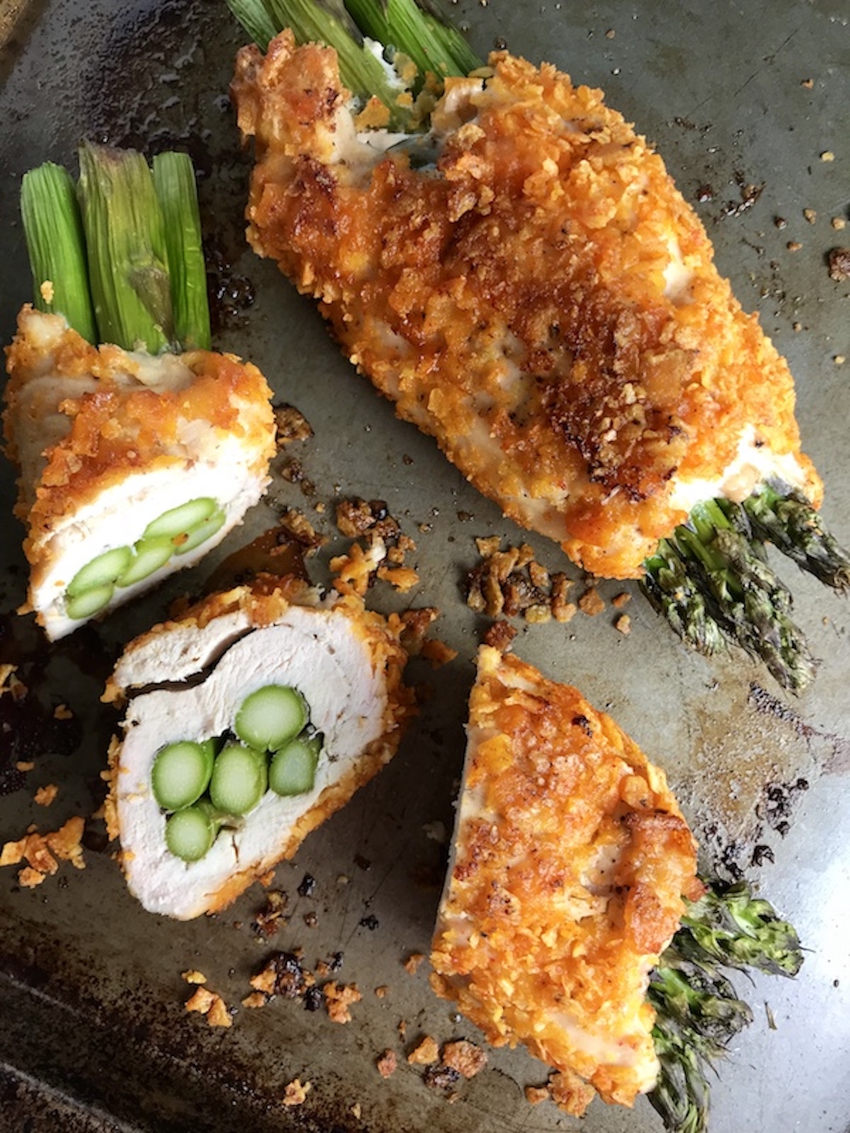 Cheese Tortilla Crusted Chicken Rolls with Asparagus on a sheet pan with one sliced.