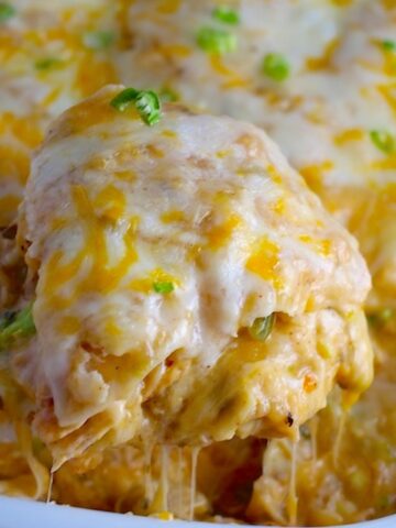 Spatula scooping Sour Cream Chicken Enchilada Casserole with zucchini. It's hearty, cheesy, delicious, & easy because everything is layered in one dish.