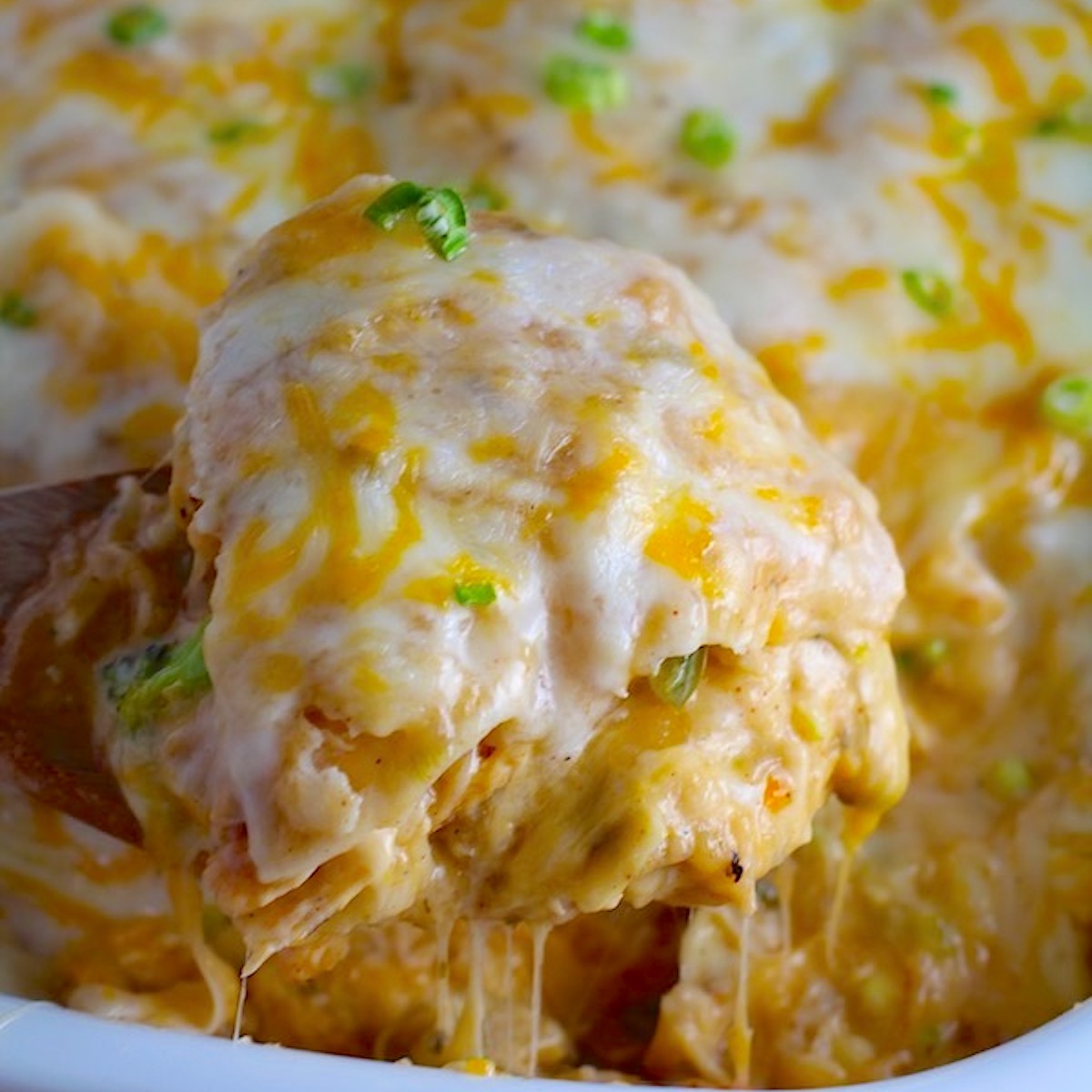 Spatula scooping Sour Cream Chicken Enchilada Casserole with zucchini. It's hearty, cheesy, delicious, & easy because everything is layered in one dish.