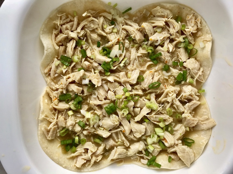 Layer of shredded chicken and scallions in pan for Sour Cream Chicken Enchilada Casserole with zucchini. It's hearty, cheesy, delicious, & easy because everything is layered in one dish.