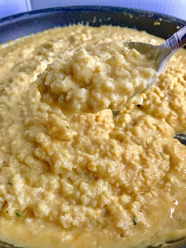 Close up picture of Cheesy Cauliflower Rice in a pan with a spoon scooping it up.